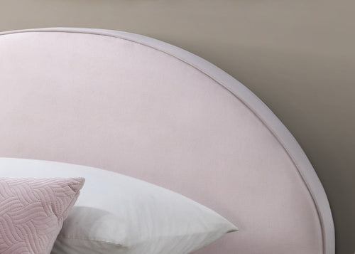 Round headboard with a soft pink finish and a white pillow on a neutral wall.